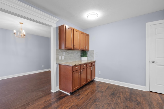 kitchen with dark wood-type flooring, hanging light fixtures, decorative backsplash, light stone countertops, and a chandelier