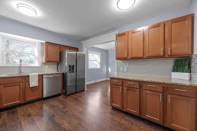 kitchen featuring appliances with stainless steel finishes, tasteful backsplash, light stone counters, and dark wood-type flooring