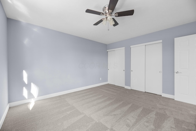 unfurnished bedroom featuring multiple closets, ceiling fan, and light carpet