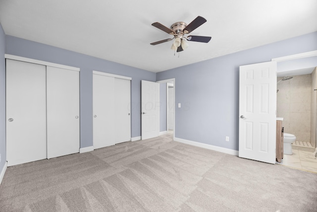 unfurnished bedroom featuring ensuite bathroom, ceiling fan, light carpet, and multiple closets