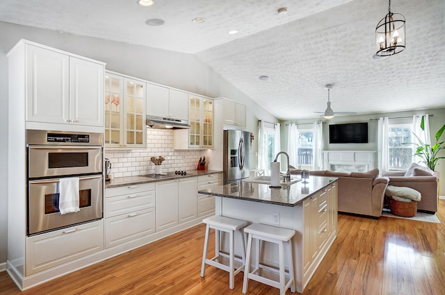 kitchen with sink, stainless steel appliances, dark stone countertops, decorative light fixtures, and a kitchen island with sink