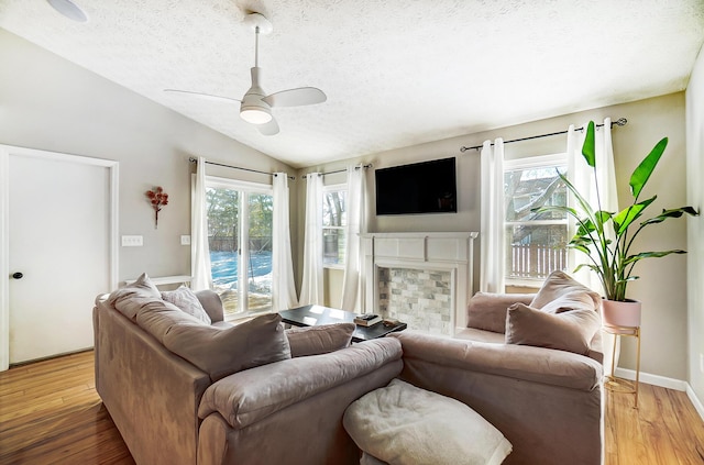 living room featuring ceiling fan, wood-type flooring, a textured ceiling, vaulted ceiling, and a fireplace