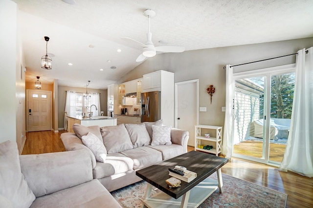 living room featuring ceiling fan, light wood-type flooring, sink, and lofted ceiling