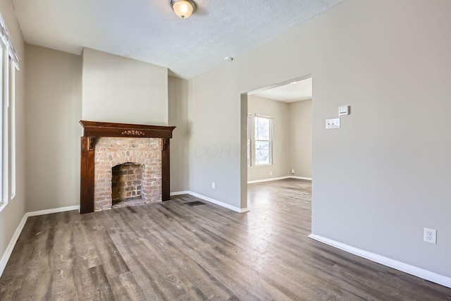 unfurnished living room featuring a brick fireplace, hardwood / wood-style flooring, and a textured ceiling