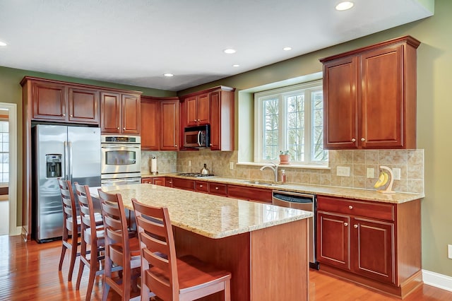 kitchen with light stone countertops, a center island, stainless steel appliances, and light hardwood / wood-style floors