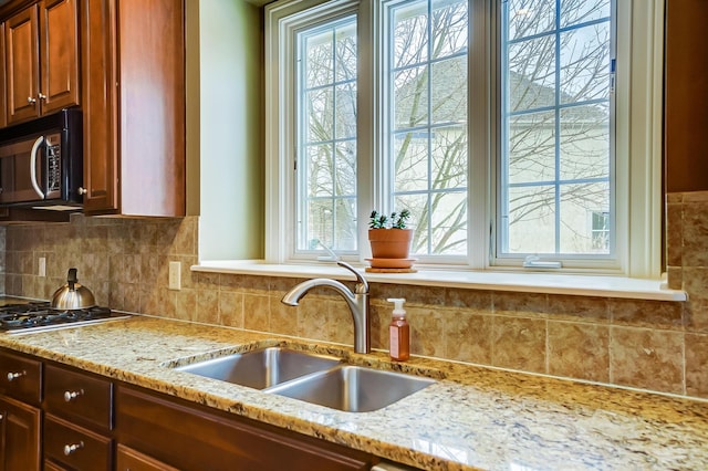 kitchen featuring tasteful backsplash, light stone counters, stainless steel gas stovetop, and sink