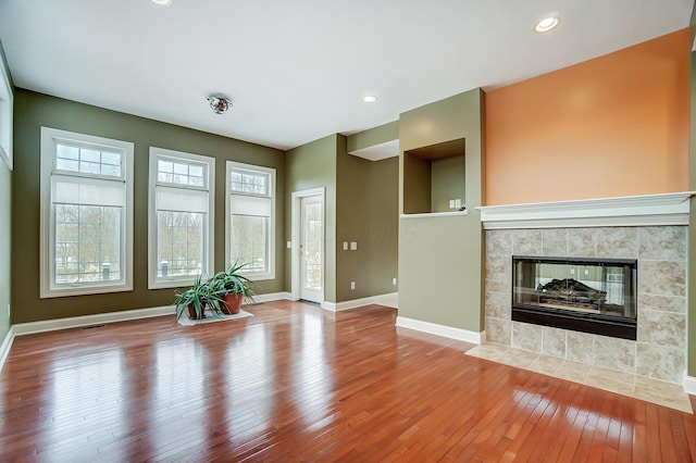 unfurnished living room with a tile fireplace, wood-type flooring, and a wealth of natural light