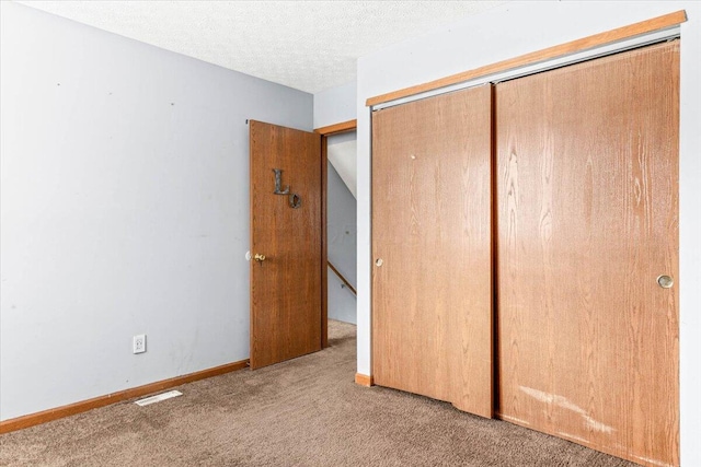 unfurnished bedroom with light colored carpet, a textured ceiling, and a closet