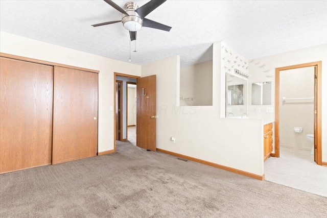 unfurnished bedroom with ensuite bathroom, a closet, ceiling fan, and light colored carpet