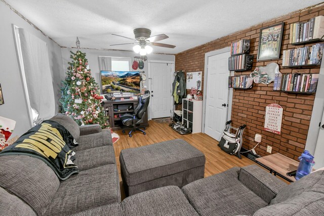 living room featuring a textured ceiling, light hardwood / wood-style flooring, ceiling fan, and brick wall