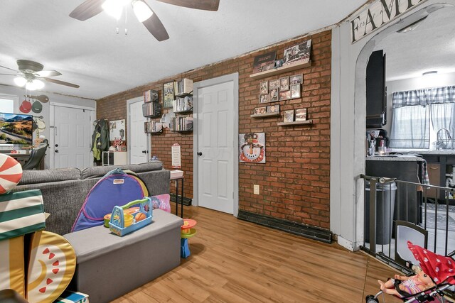 living room featuring sink, a textured ceiling, light wood-type flooring, and brick wall