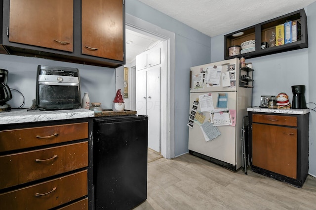 kitchen featuring dark brown cabinetry, white fridge, fridge, a textured ceiling, and light wood-type flooring