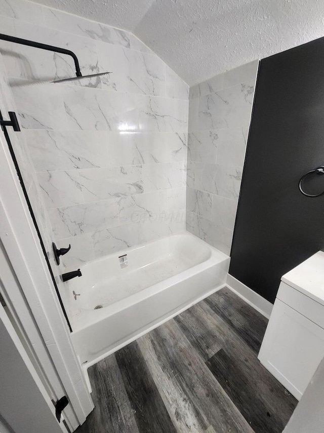 bathroom with a textured ceiling, hardwood / wood-style flooring, vaulted ceiling, and shower / washtub combination