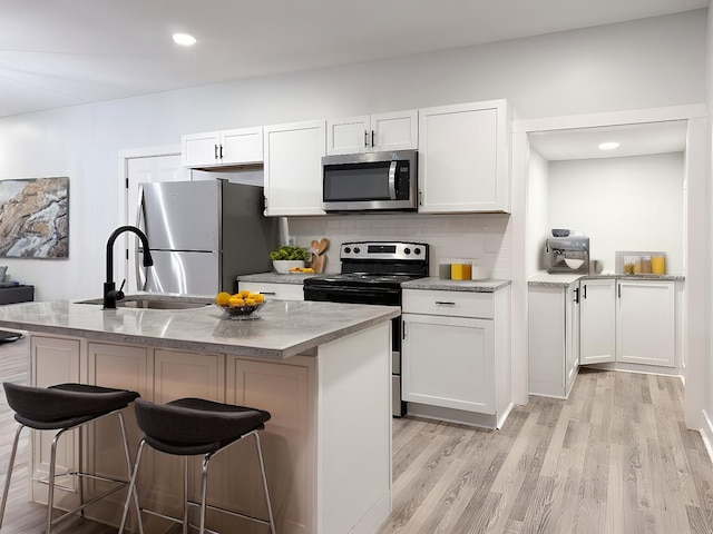 kitchen featuring appliances with stainless steel finishes, white cabinetry, an island with sink, sink, and backsplash