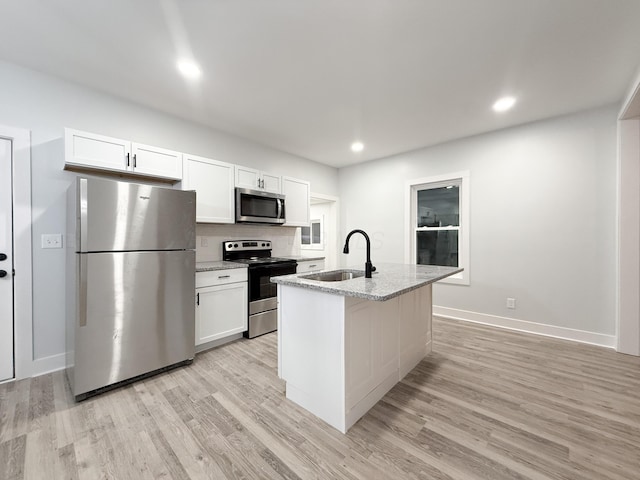 kitchen with sink, white cabinetry, a kitchen island with sink, stainless steel appliances, and light stone countertops