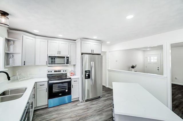 kitchen with sink, stainless steel appliances, light stone counters, white cabinets, and light wood-type flooring