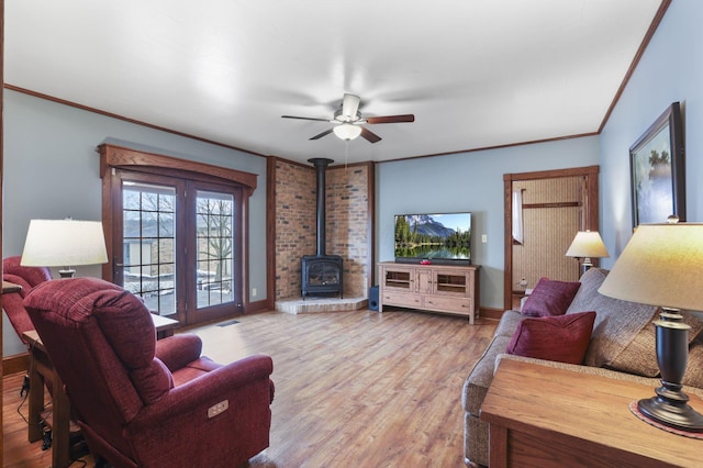 living area featuring french doors, ornamental molding, a wood stove, wood finished floors, and baseboards