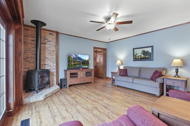 living area featuring visible vents, a ceiling fan, light wood-style flooring, a wood stove, and crown molding