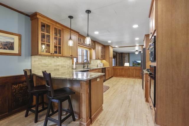 kitchen with a peninsula, a sink, light stone countertops, light wood finished floors, and brown cabinetry