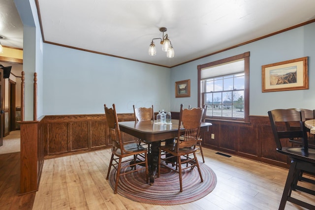 dining room with a chandelier, wood walls, visible vents, light wood-type flooring, and wainscoting