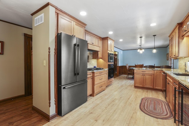 kitchen featuring stainless steel appliances, a peninsula, a sink, and light wood-style floors