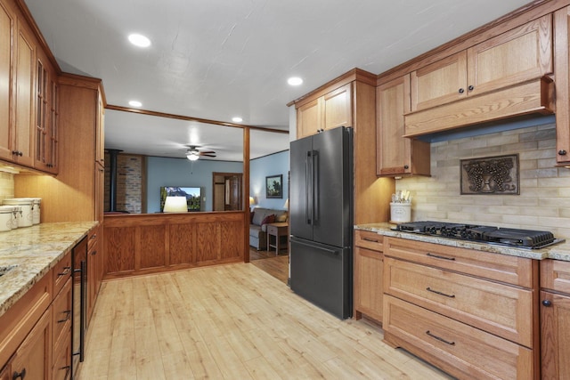 kitchen with black appliances, light stone counters, light wood-type flooring, and backsplash