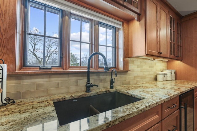 kitchen featuring brown cabinets, decorative backsplash, glass insert cabinets, a sink, and light stone countertops