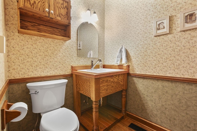 bathroom with a wainscoted wall, wood finished floors, toilet, and wallpapered walls