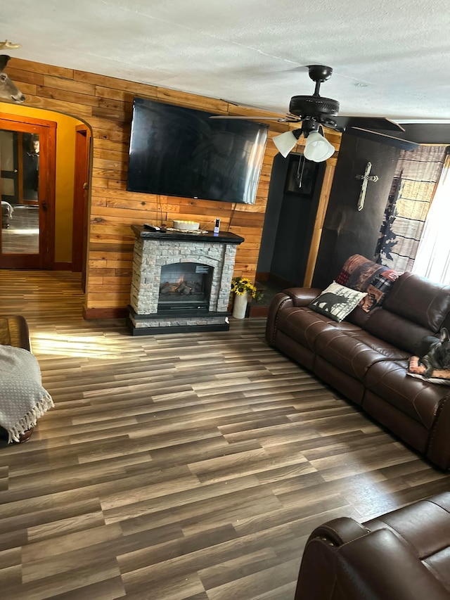 living room with a textured ceiling, dark hardwood / wood-style floors, wood walls, a fireplace, and ceiling fan