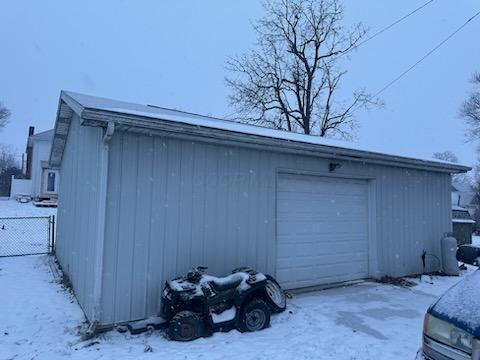 snow covered garage featuring a detached garage and fence