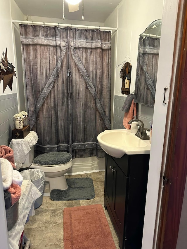 full bath featuring curtained shower, a wainscoted wall, toilet, vanity, and tile walls