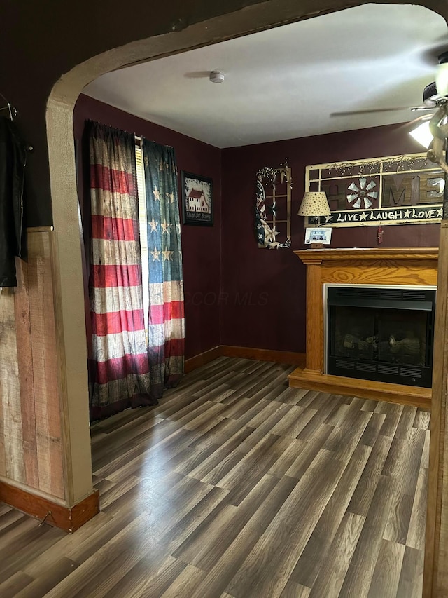 unfurnished living room featuring baseboards, arched walkways, ceiling fan, a fireplace, and wood finished floors