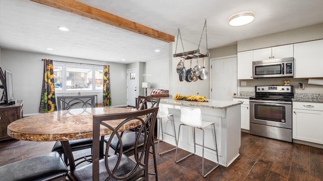 kitchen featuring a kitchen bar, light stone countertops, stainless steel appliances, dark hardwood / wood-style floors, and white cabinetry