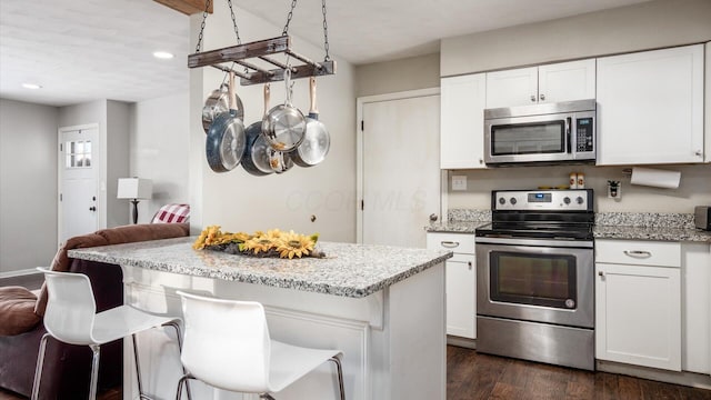 kitchen featuring white cabinets, appliances with stainless steel finishes, light stone countertops, and a breakfast bar area