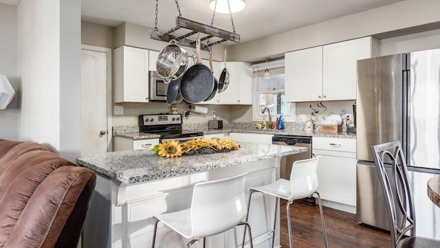 kitchen featuring light stone countertops, appliances with stainless steel finishes, dark wood-type flooring, a center island, and white cabinetry