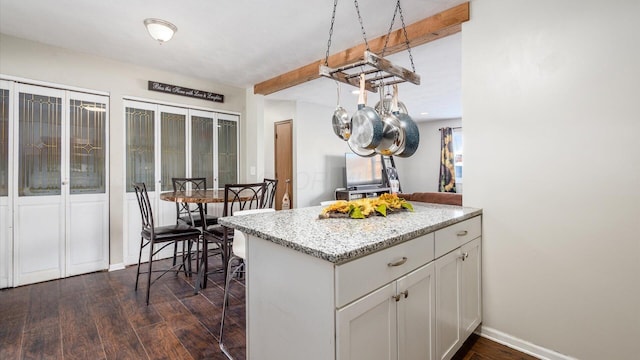 kitchen featuring white cabinetry, light stone countertops, dark hardwood / wood-style flooring, beamed ceiling, and kitchen peninsula