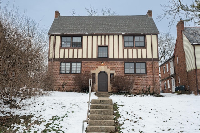 tudor home featuring brick siding, roof with shingles, and a chimney