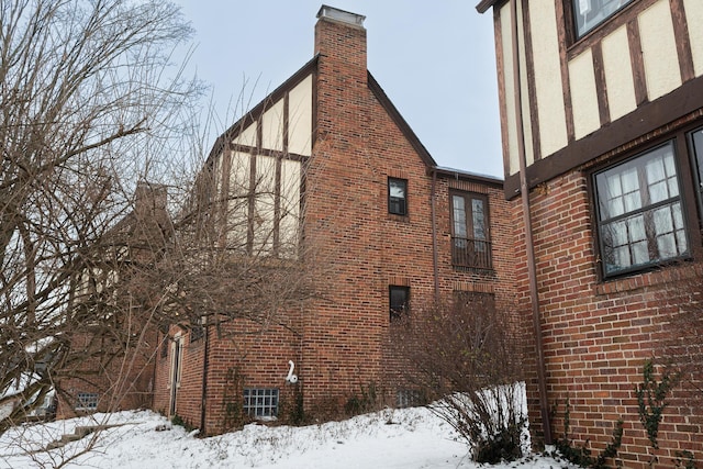 view of snow covered exterior featuring brick siding and a chimney