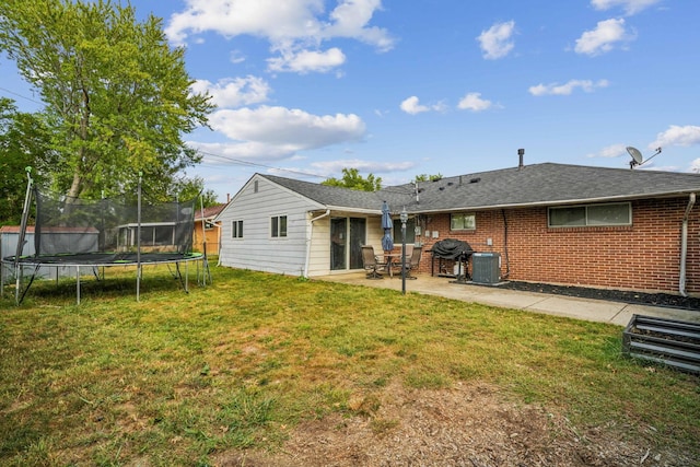 rear view of property with a trampoline, central AC unit, a patio area, and a lawn