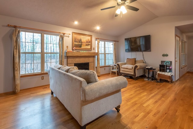 living room with vaulted ceiling, light hardwood / wood-style flooring, ceiling fan, and a tiled fireplace