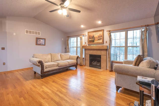 living room with a textured ceiling, vaulted ceiling, ceiling fan, light hardwood / wood-style flooring, and a tiled fireplace