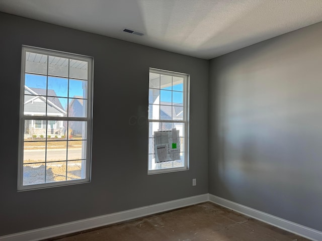 unfurnished room featuring visible vents, baseboards, a textured ceiling, and a healthy amount of sunlight