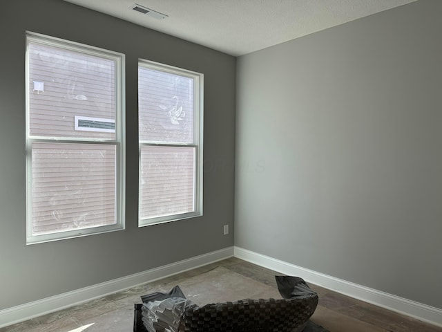 empty room featuring visible vents, a textured ceiling, and baseboards