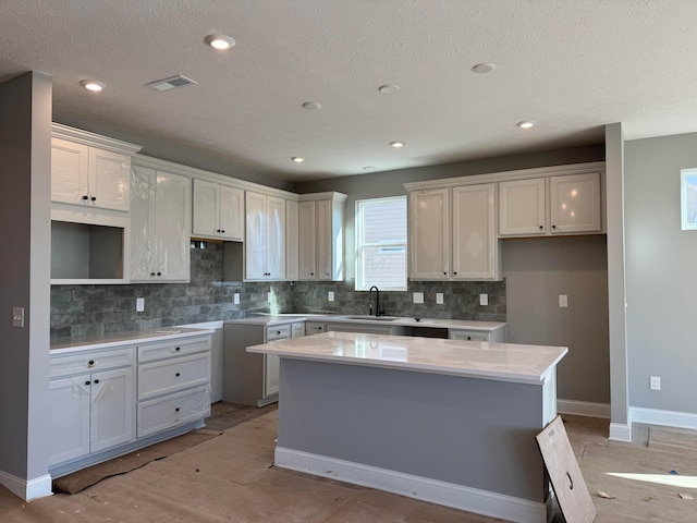 kitchen with visible vents, a sink, a center island, decorative backsplash, and baseboards