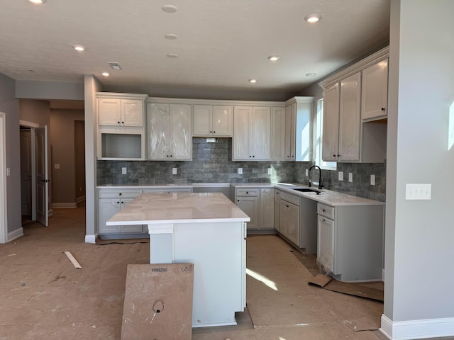 kitchen featuring backsplash, a center island, baseboards, and a sink