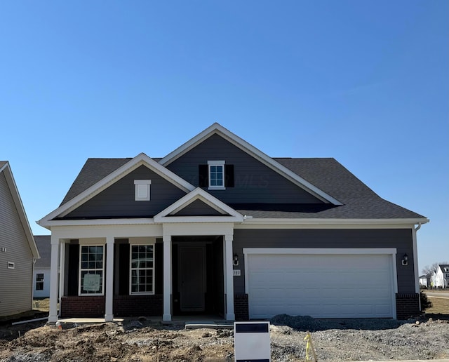 view of front of property featuring brick siding, a porch, a shingled roof, and a garage