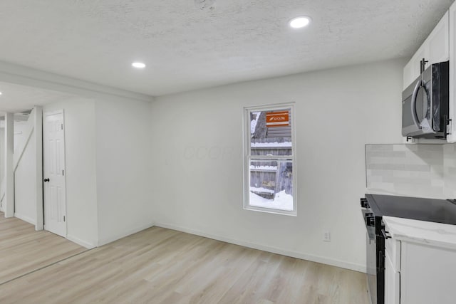 kitchen with backsplash, range, light wood-type flooring, a textured ceiling, and white cabinetry