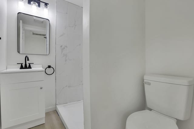 bathroom featuring hardwood / wood-style flooring, vanity, toilet, and a tile shower