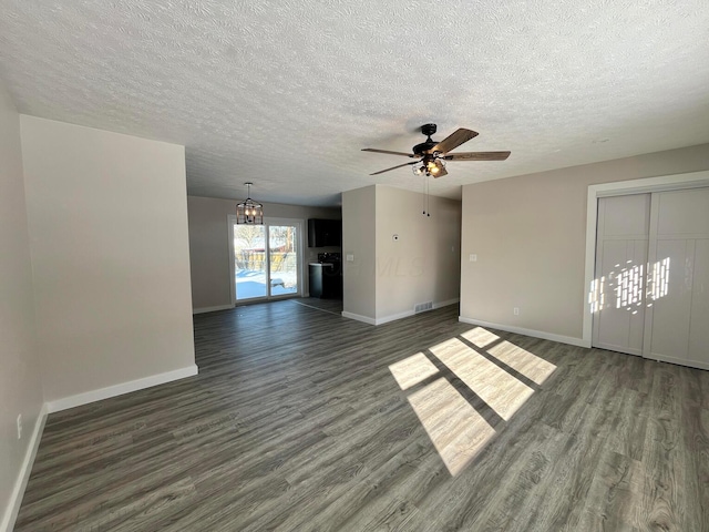 unfurnished living room with a textured ceiling, dark wood-type flooring, and ceiling fan with notable chandelier