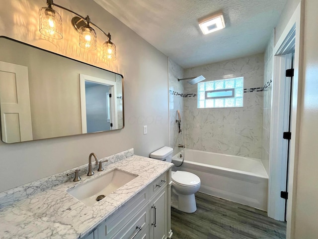 full bathroom featuring hardwood / wood-style floors, vanity, tiled shower / bath combo, toilet, and a textured ceiling